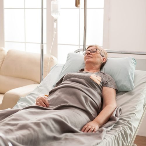 Mature lonely woman laying on bed in a nursing home covered with a blanket.